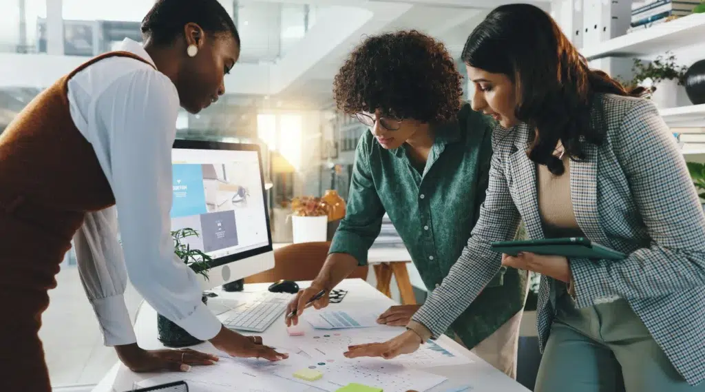 Three colleagues gather around a monitor and paperwork, collaborating on the implementation of an AI-driven operations strategy.